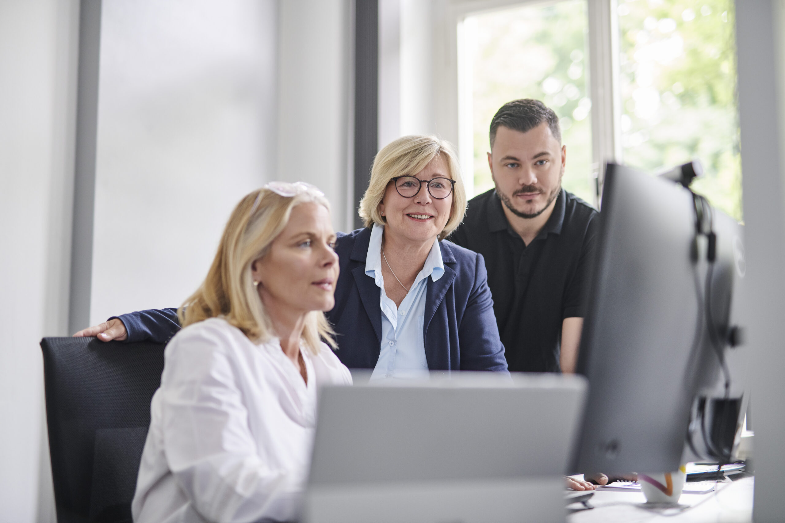 Drei Personen arbeiten gemeinsam im Büro an einem Computerbildschirm, eine Frau tippt, während die anderen konzentriert zusehen