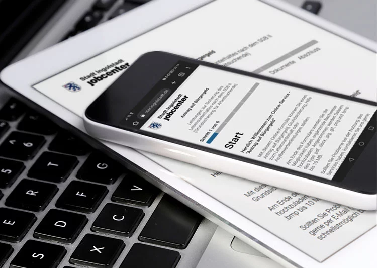 Digitalisierung in der öffentlichen Verwaltung – Smartphone und Tablet mit Online-Formular des Jobcenters auf Laptop-Tastatur, symbolisch für E-Government und digitale Services.
