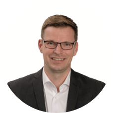 Geschäftsmann im Anzug lächelt vor weißem Hintergrund – professionelles Porträtfoto für Unternehmenswebsite.